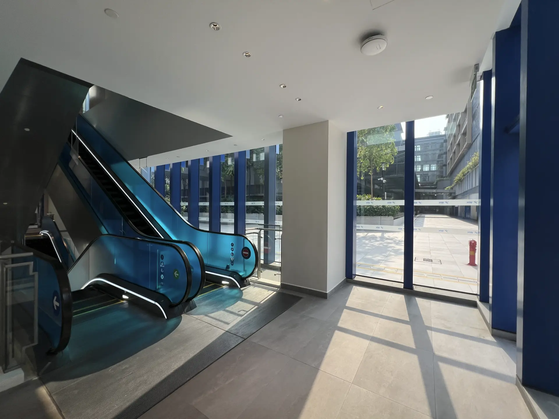 Escalator hall with daylight streaming through tall glazing and casting shadows across the floor